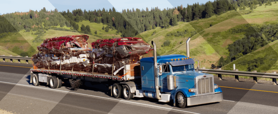 A loaded flatbed on the highway with rolling hills in the background.