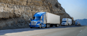 three trucks driving down the highway next to a mountainside