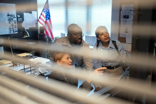 Group of FBI agents in formalwear discussing behavior of criminal while watching record from security camera inside office.