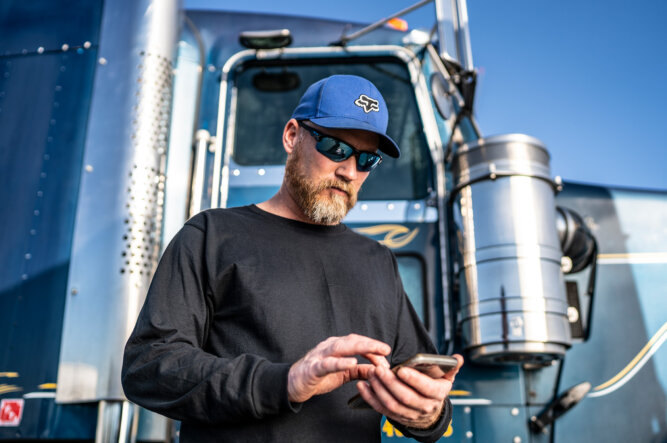Man standing in front of a semi truck, looking at his cell phone