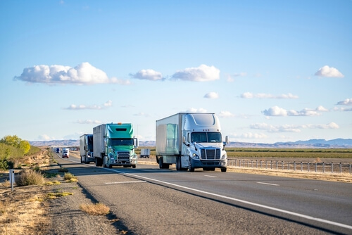 Several semi trucks driving down a highway in a remote area.